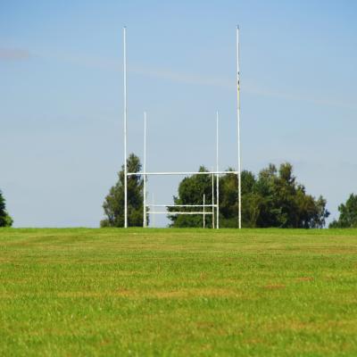 a photo of a field. the sky is blue. Rugby posts stand in front of trees