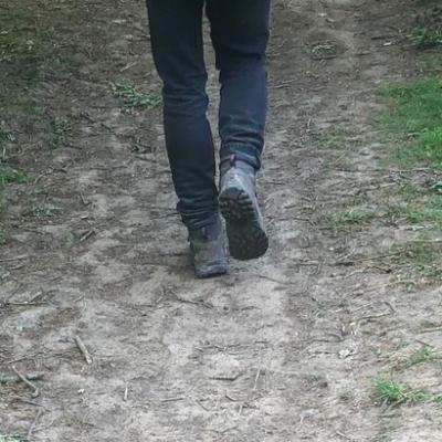 a mans boots and lower legs.  He is walking away from the camera on a mud path