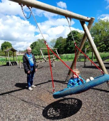 a child sits on a rope mesh swing, an older man stands behind smiling