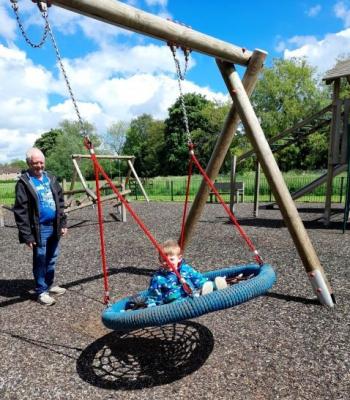 a young boy is sitting on a flat mesh swing, smiling while an older man stands behind