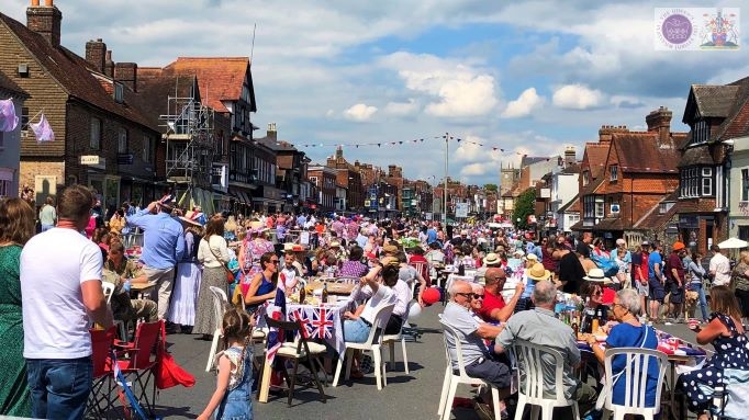 A street scene.  A wide street is packed with people sitting at tables or standing, most wearing red, white and blue