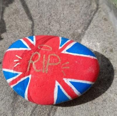 a pebble painted in red white and blue with RIP written in gold
