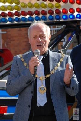 A man wearing a jacket and chain of office speaks into a microphone