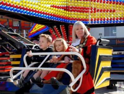a woman wearing mayoral robes and two children sit in a fairground ride