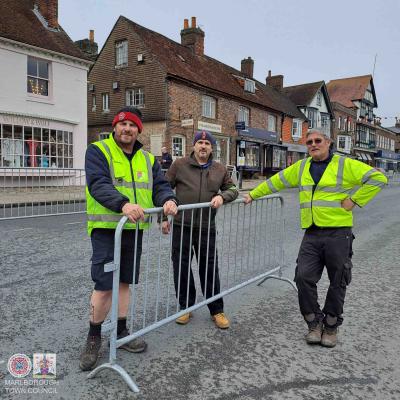 three men stand with a metal barrier. 2 wear hi viz clothing